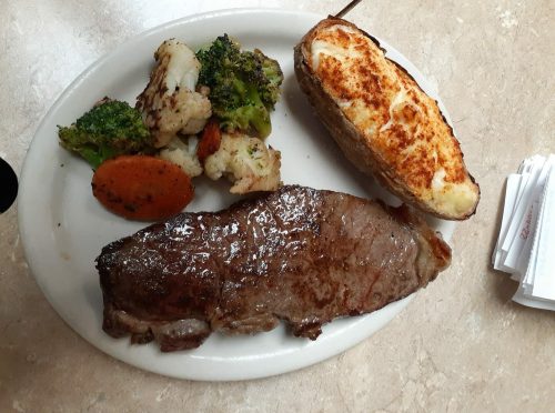 A plate featuring a grilled steak, baked potato, and a side of mixed vegetables including broccoli and cauliflower.