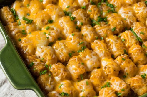 A close-up of a cheesy tater tot casserole topped with green onions in a green baking dish.