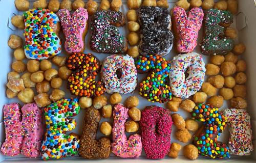 A colorful assortment of donuts and mini donuts arranged to say "BYE 2020" and "HELLO 2021" with sprinkles.
