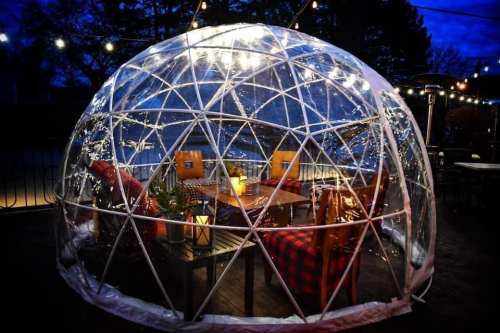 A cozy outdoor dining igloo with string lights, a table, and chairs, set against a twilight sky.