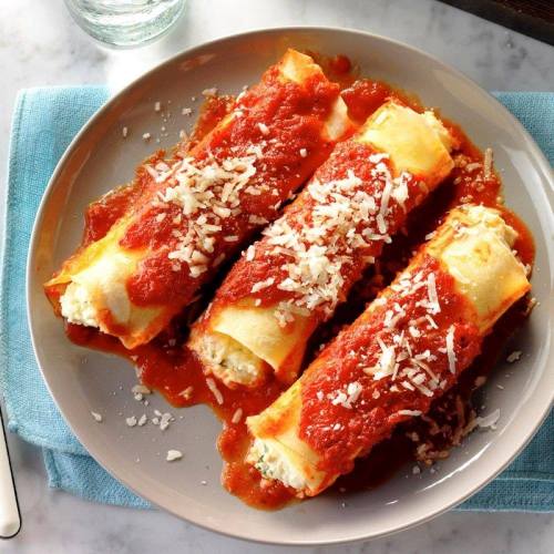 Three cheese-filled cannelloni topped with marinara sauce and grated cheese, served on a plate with a blue napkin.