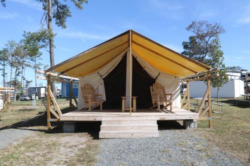 A glamping tent with a wooden deck and two Adirondack chairs, set in a grassy area with trees in the background.