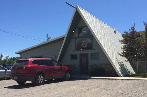 A red SUV parked in front of a unique A-frame building with a green roof and stone accents on a sunny day.