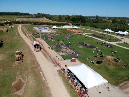 Aerial view of a lively outdoor event with tents, play areas, and people enjoying activities on a sunny day.