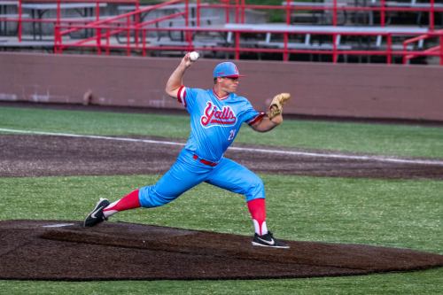 A baseball player in a blue and red uniform pitches on the mound during a game.