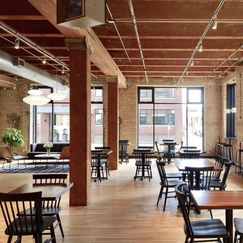 Bright, spacious restaurant interior with wooden beams, tables, and chairs, featuring large windows and a cozy atmosphere.