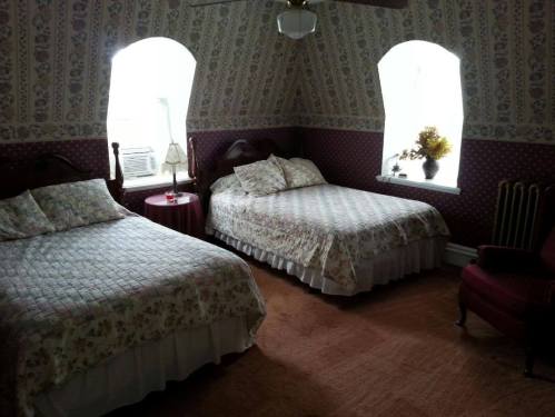 Cozy bedroom with two floral-patterned beds, a small table, and a vintage armchair under a sloped ceiling.