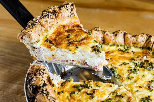 A slice of savory pie with a golden crust, cheese, and herbs being lifted from a pie dish.