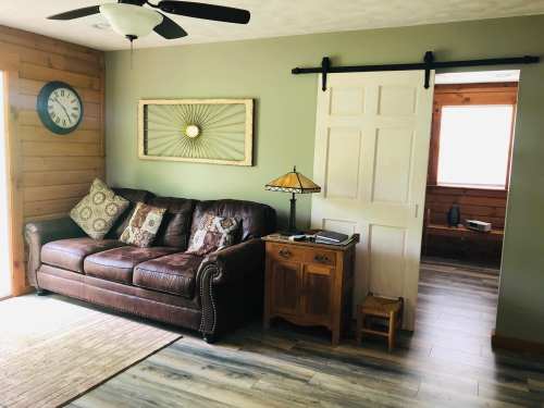 Cozy living room with a leather sofa, decorative pillows, a wooden side table, and a sliding door. Natural light from a window.