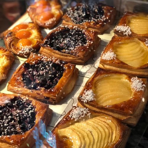 A display of assorted pastries with fruit fillings, including blueberry, apricot, and pear, topped with sugar crystals.