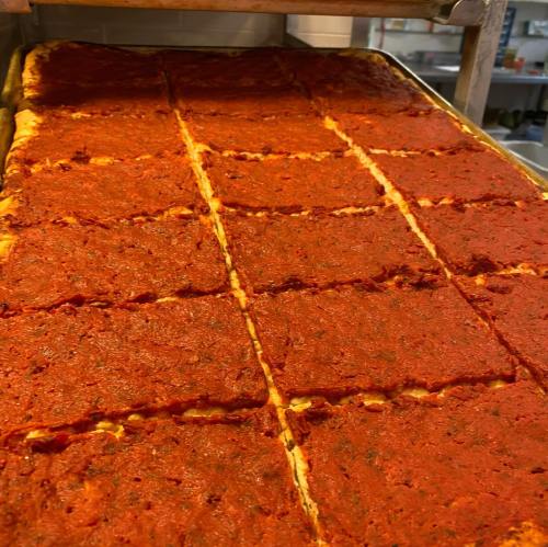 A tray of freshly baked pizza, cut into square slices, topped with a rich red sauce.