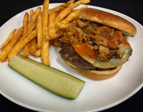 A plate featuring a burger topped with pulled meat and cheese, served with fries and a pickle on the side.