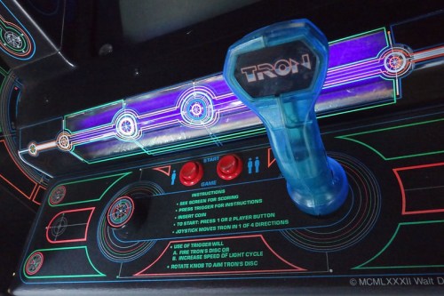 Close-up of a vintage arcade game control panel featuring a blue joystick and colorful, illuminated graphics.