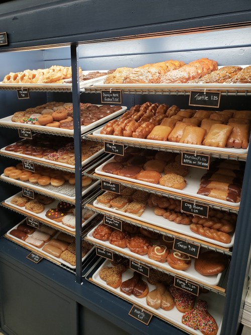A display case filled with various types of donuts and pastries, neatly arranged on shelves.