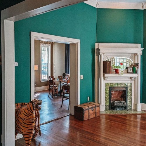 A cozy room with teal walls, a fireplace, and a tiger statue near an open doorway leading to another room.