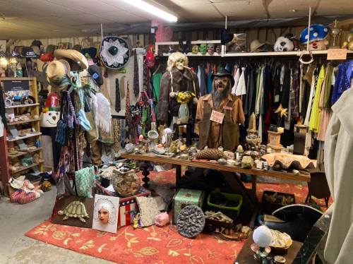 A cluttered vintage shop filled with clothing, hats, and eclectic decor items on display.