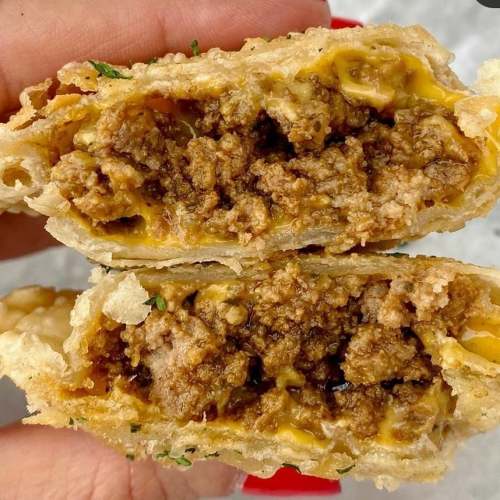 A hand holding a split pastry filled with seasoned ground meat and melted cheese, garnished with herbs.