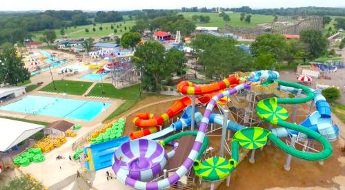 Aerial view of a vibrant water park featuring colorful slides, pools, and amusement rides surrounded by greenery.