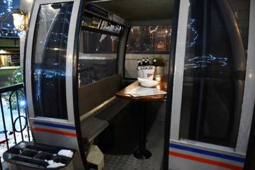 A cozy, enclosed dining booth with a table and seating, decorated with lights and a bucket of drinks.