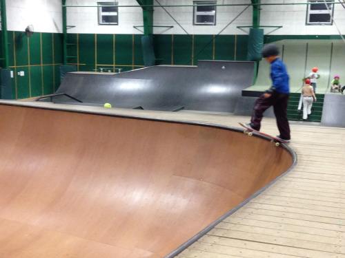 A skateboarder performs a trick on a curved ramp in an indoor skate park.