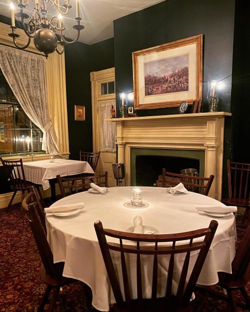Cozy dining room with a round table set for four, elegant decor, a fireplace, and a large framed painting on the wall.
