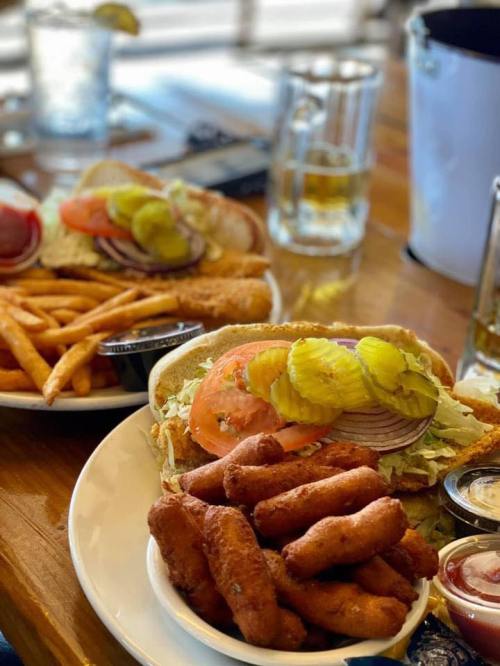 A plate of crispy fried food, including chicken tenders and fries, with a sandwich topped with lettuce, tomato, and pickles.