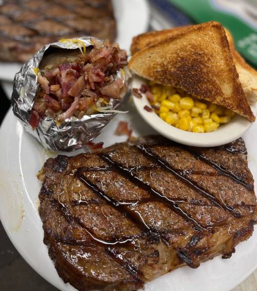 A plate featuring a grilled steak, baked potato with bacon, corn, and toasted bread.