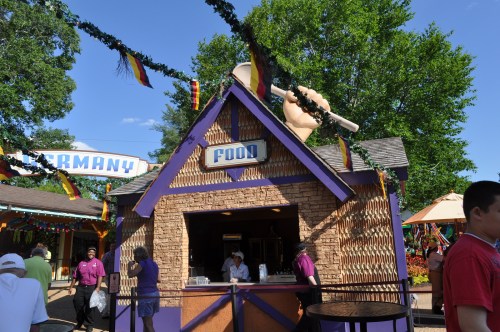 A colorful food stand with a large spoon decoration, surrounded by festive decorations and people enjoying the atmosphere.