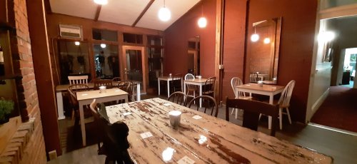 Cozy restaurant interior with wooden tables, chairs, and warm lighting, featuring large windows and a rustic ambiance.