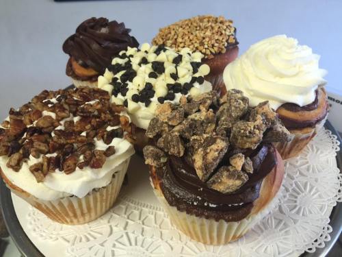 A variety of decorated cupcakes with chocolate, nuts, and cream toppings on a decorative plate.