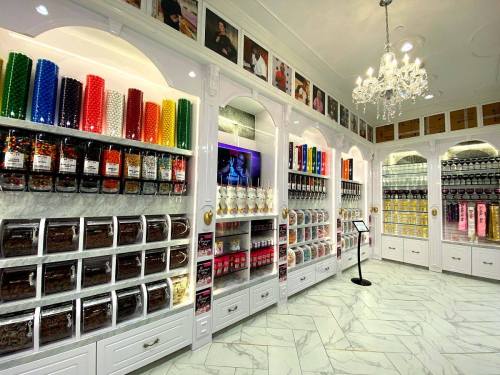 A colorful candy store interior with jars and bins filled with various sweets, featuring elegant white cabinetry and decor.