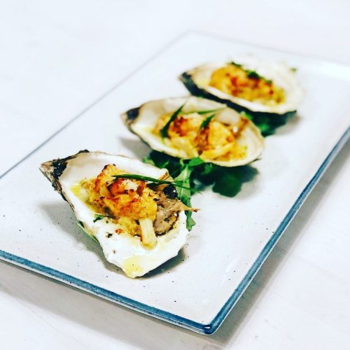 Three baked oysters topped with a golden crust, served on a white plate with a garnish of greens.