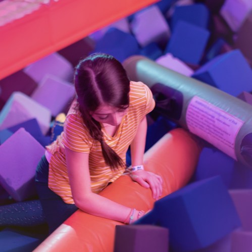 A girl in a striped shirt climbs over colorful foam blocks in a play area.