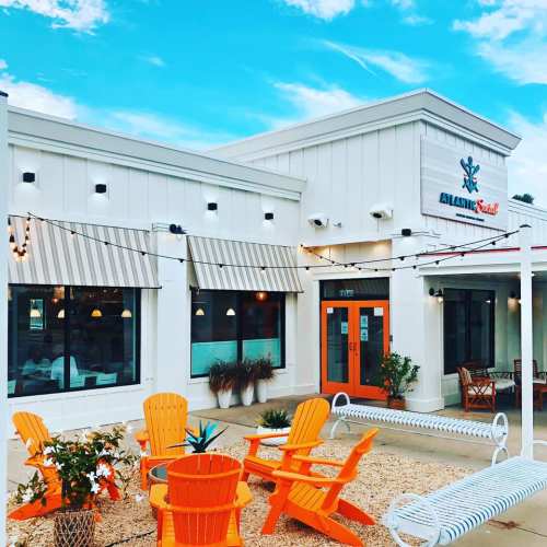 Brightly colored outdoor seating area in front of a modern restaurant with a blue sky and decorative string lights.