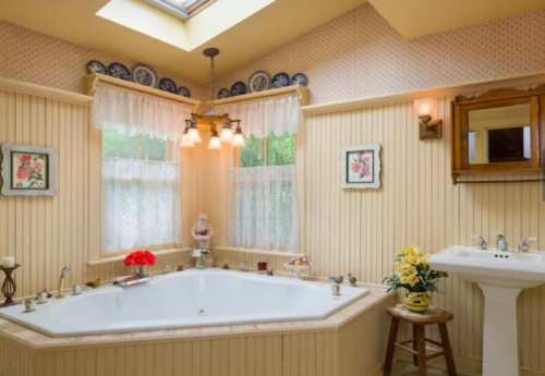 Cozy bathroom with a large tub, skylight, decorative plates, and floral accents. Bright and inviting atmosphere.