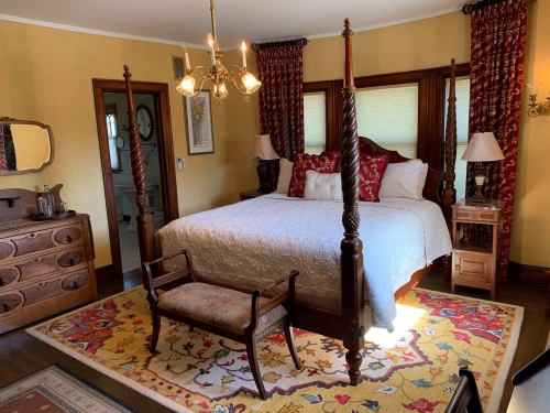 A cozy bedroom featuring a four-poster bed, decorative pillows, a wooden dresser, and a colorful area rug.