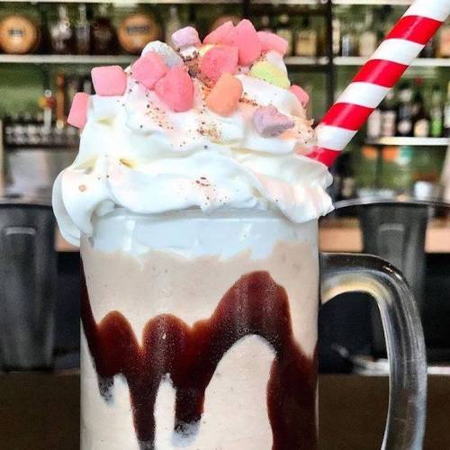 A creamy milkshake topped with whipped cream, colorful marshmallows, and a red and white striped straw.