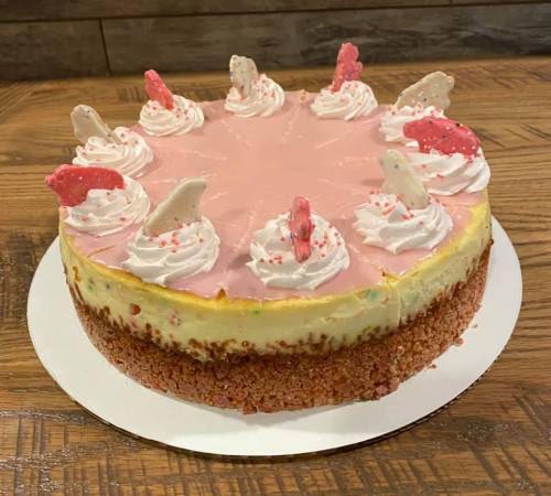 A pink frosted cake with whipped cream swirls and decorative candy on top, set on a wooden table.