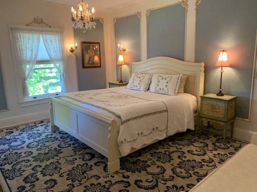 A cozy bedroom featuring a white bed, elegant decor, a chandelier, and soft blue walls.