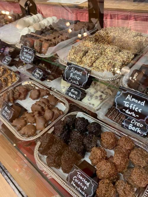 A display case filled with various chocolates and confections, labeled with names like "Almond Butter Crunch" and "Toasted Coconut."