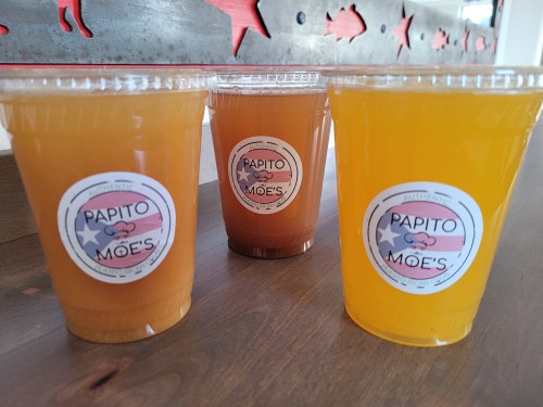 Three clear cups filled with colorful beverages, each labeled "Papito Moe's," on a wooden table.