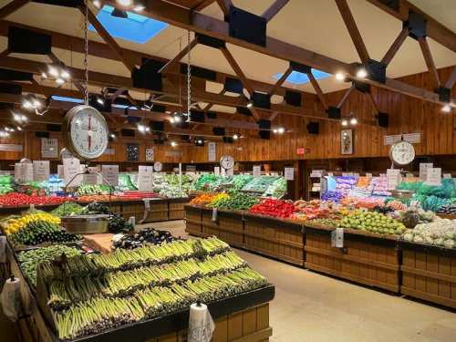 A vibrant produce market with colorful fruits and vegetables displayed on wooden tables under warm lighting.