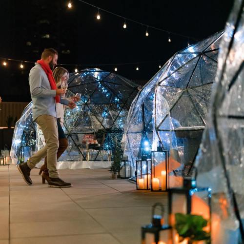 A couple walks through illuminated igloo-like structures, surrounded by candles and string lights at night.