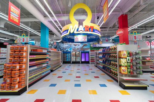 Brightly lit grocery store aisle with colorful shelves, featuring snacks and drinks, and a large "MART" sign overhead.