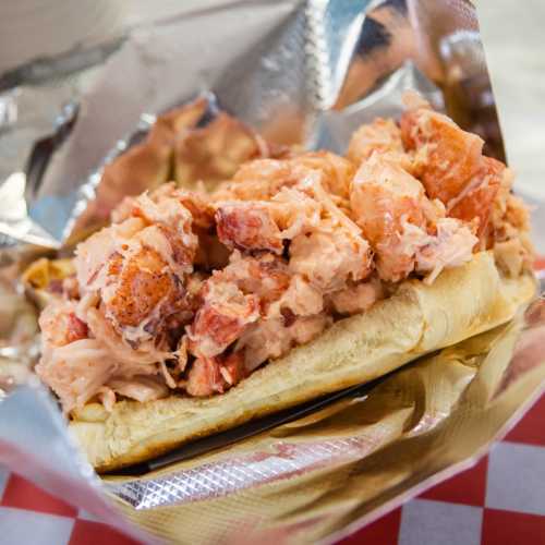 A lobster roll filled with chunks of lobster meat, served in a toasted bun and wrapped in foil.