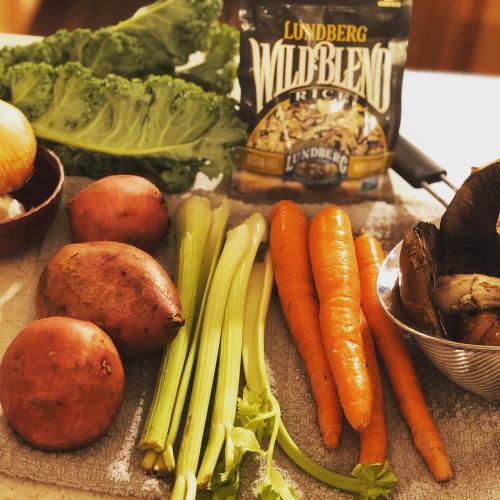 A variety of fresh vegetables including potatoes, carrots, celery, and kale, alongside a package of rice blend.