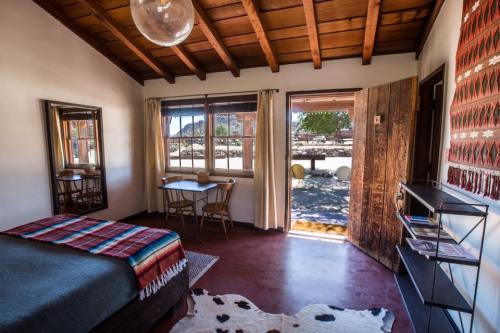 Cozy bedroom with wooden ceiling, a bed, table, and door leading to an outdoor view. Decorated with a colorful blanket.
