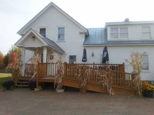 A white house with a wooden deck, decorated with corn stalks and flowers, under a cloudy sky.