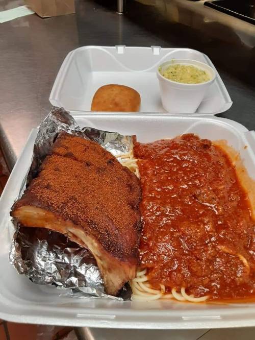 A takeout container with ribs, spaghetti in marinara sauce, a roll, and a side of coleslaw.