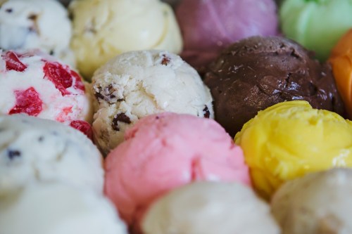 A colorful assortment of ice cream scoops in various flavors, including pink, yellow, brown, and green.